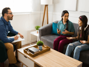 A family therapist sits with a mother and daughter during a counseling session in a bright, modern office. Family therapy can help individuals within a family find solutions to their problems together. Looks for a family therapist in Scotch Plains or Branchburg today!