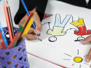 Child's hands drawing colorful depictions of their family with crayons on paper. Bringing the family together in family therapy can be helpful to resolve family struggles. Look for a family therapist in New Jersey today!