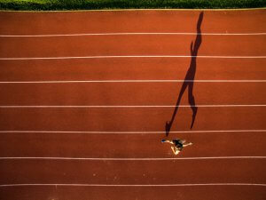 A top down view of a track runner and their long shadow. Learn how therapy for teens in Branchburg, NJ can offer support for young athletes by searching for online therapy in New Jersey or “therapist branchburg, nj”. They can offer support via online therapy for teens and more.