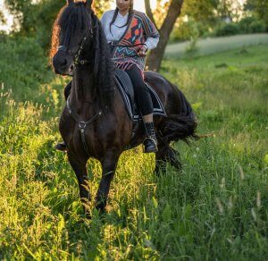 A woman rides a black horse through a lush green field, dressed in a colorful poncho and black riding boots. This could represent the bonds cultivated with equestrian therapy in New Jersey. Learn how to redefine your identity by contacting an equestrian therapist Branchburg, NJ or searching for an EMDR therapist in Somerville, NJ.