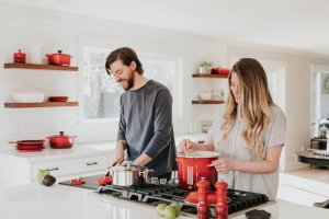 A couple cooking together in a kitchen with red cookware, demonstrating supportive partnership while managing food allergy anxiety. Therapy in Scotch Plains NJ helps couples develop strategies for advocating and supporting each other through food allergy challenges