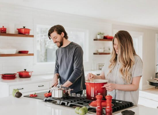 A couple cooking together in a modern kitchen with red cookware, demonstrating supportive partnership while managing food allergy anxiety. Therapy in Scotch Plains NJ helps couples develop strategies for advocating and supporting each other through food allergy challenges.
