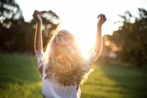 A backlit photograph of a person with curly hair raising their arms in celebration against a sunset background, representing the freedom and joy that comes from therapeutic support for neurodivergent individuals reclaiming their identity and sexuality in Scotch Plains and surrounding areas.