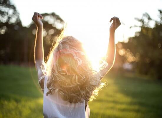 A backlit photograph of a person with curly hair raising their arms in celebration against a sunset background, representing the freedom and joy that comes from therapeutic support for neurodivergent individuals reclaiming their identity and sexuality in Scotch Plains and surrounding areas.