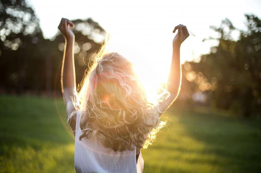 A backlit photograph of a person with curly hair raising their arms in celebration against a sunset background, representing the freedom and joy that comes from therapeutic support for neurodivergent individuals reclaiming their identity and sexuality in Scotch Plains and surrounding areas.