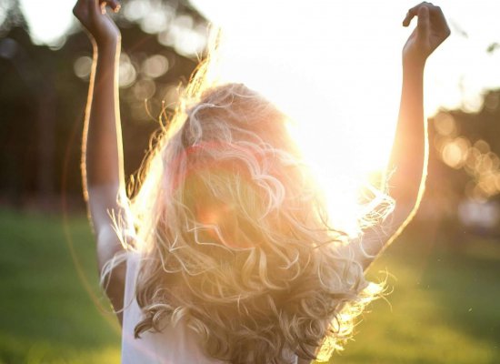 A backlit photograph of a person with curly hair raising their arms in celebration against a sunset background, representing the freedom and joy that comes from therapeutic support for neurodivergent individuals reclaiming their identity and sexuality in Branchburg and surrounding areas.