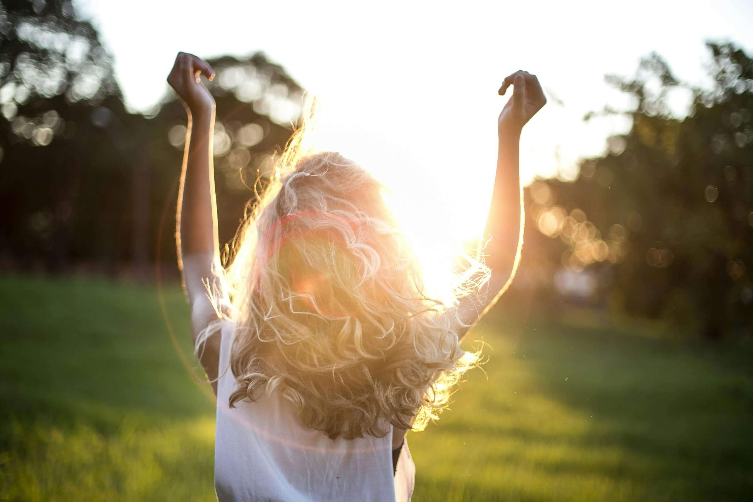 A backlit photograph of a person with curly hair raising their arms in celebration against a sunset background, representing the freedom and joy that comes from therapeutic support for neurodivergent individuals reclaiming their identity and sexuality in Scotch Plains and surrounding areas.