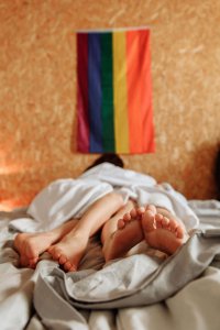 An intimate image showing feet of two people in bed with a rainbow pride flag on the wall, symbolizing how therapy services in Scotch Plains NJ creates safe spaces for neurodivergent individuals to explore and reclaim their sexuality and intimate relationships in an affirming environment.