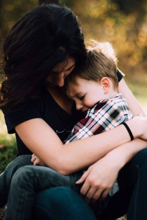 Woman sitting outdoors holding a young boy in her arms as he rests his head on her chest; both appear calm and close, sharing a quiet moment that helps regulate emotions.