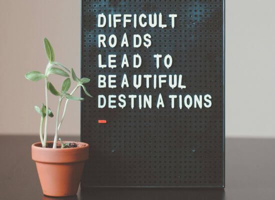 A small potted plant sits next to a black sign that reads, "Difficult roads lead to beautiful destinations.