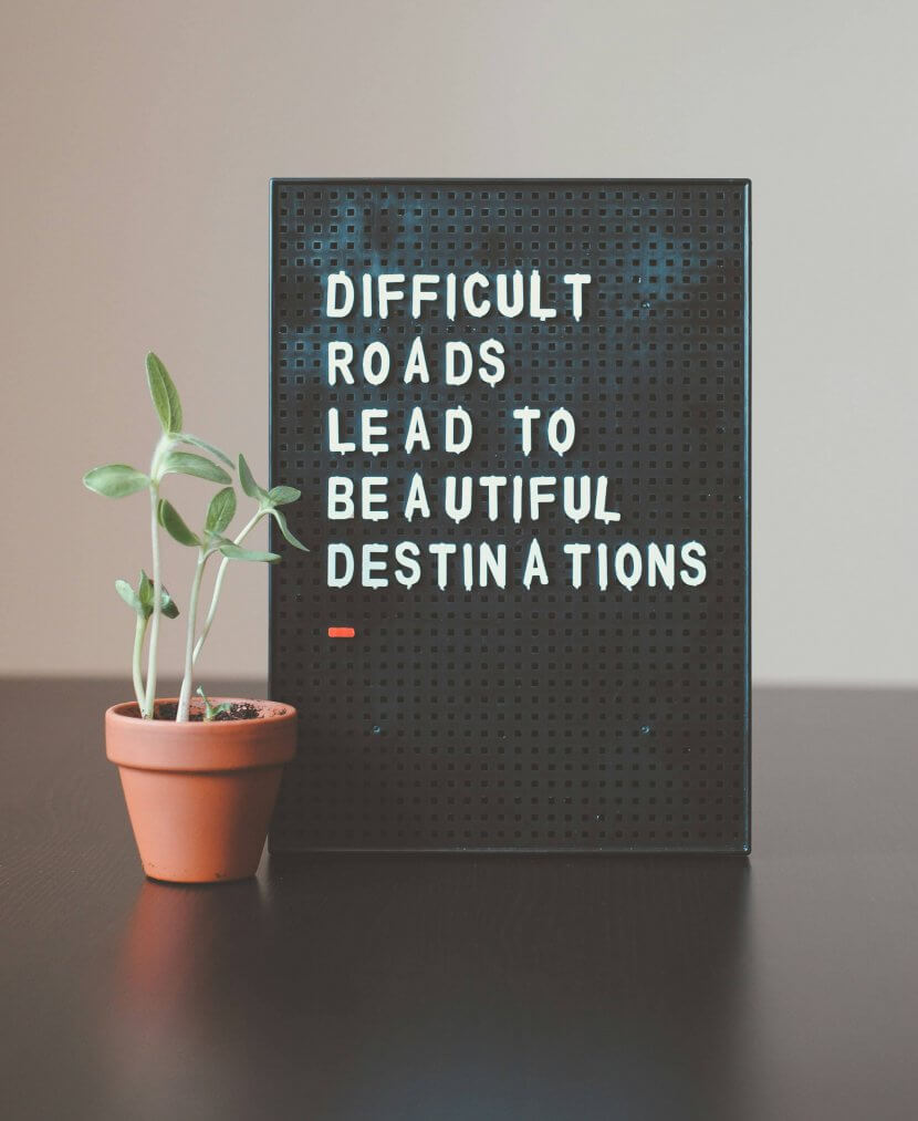 A small potted plant sits next to a black sign that reads, "Difficult roads lead to beautiful destinations.