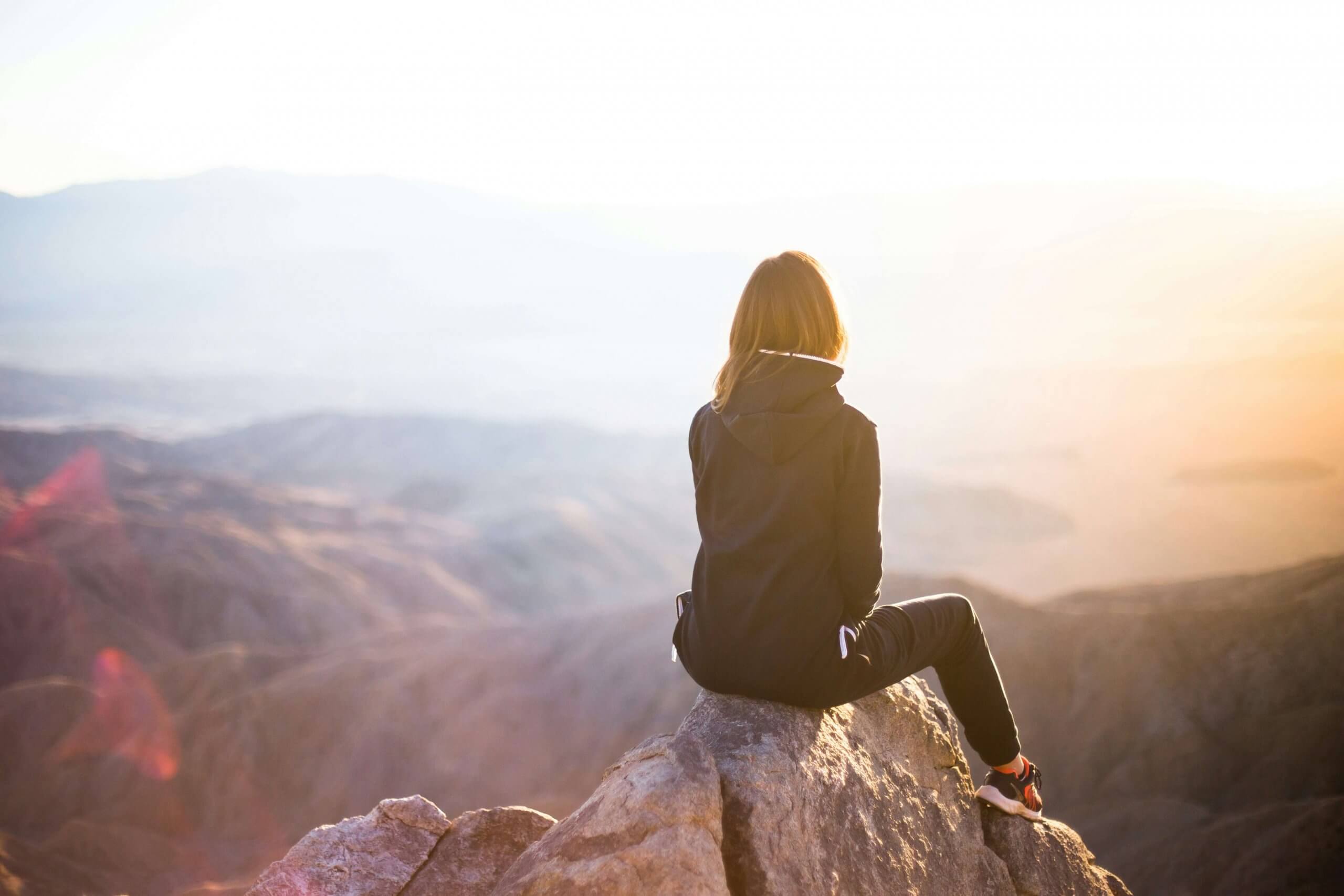 A woman sits alone on a mountain rock, looking out over the sunrise. This image represents the emotional ups and downs of the pregnancy journey in NJ, with hopeful moments of reflection and strength. Serving families in Scotch Plains, NJ Westfield , and surrounding areas.