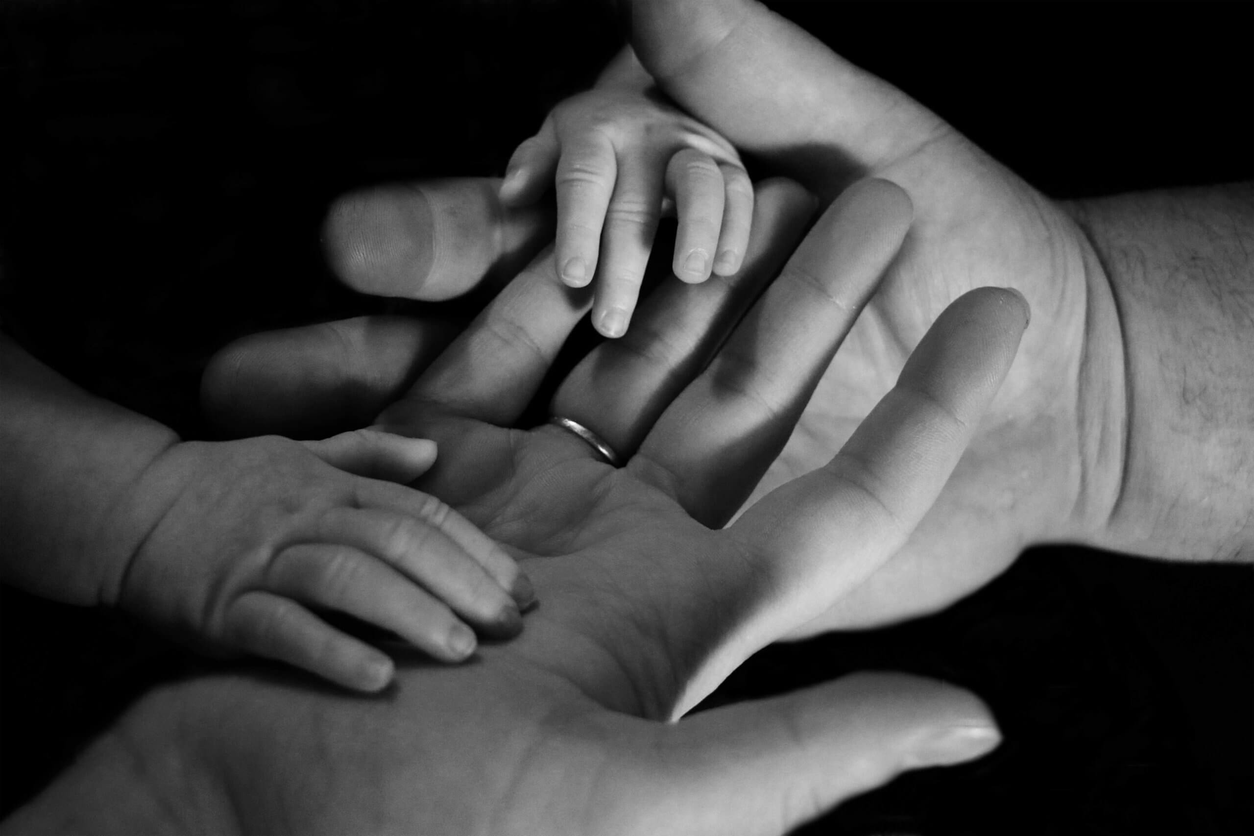 A tender black and white photograph showing adult and child hands clasped together, symbolizing family bonds and support during difficult times. Child therapist and child counseling services in Scotch Plains, NJ (07076) help families navigate loss and grief with compassionate care.