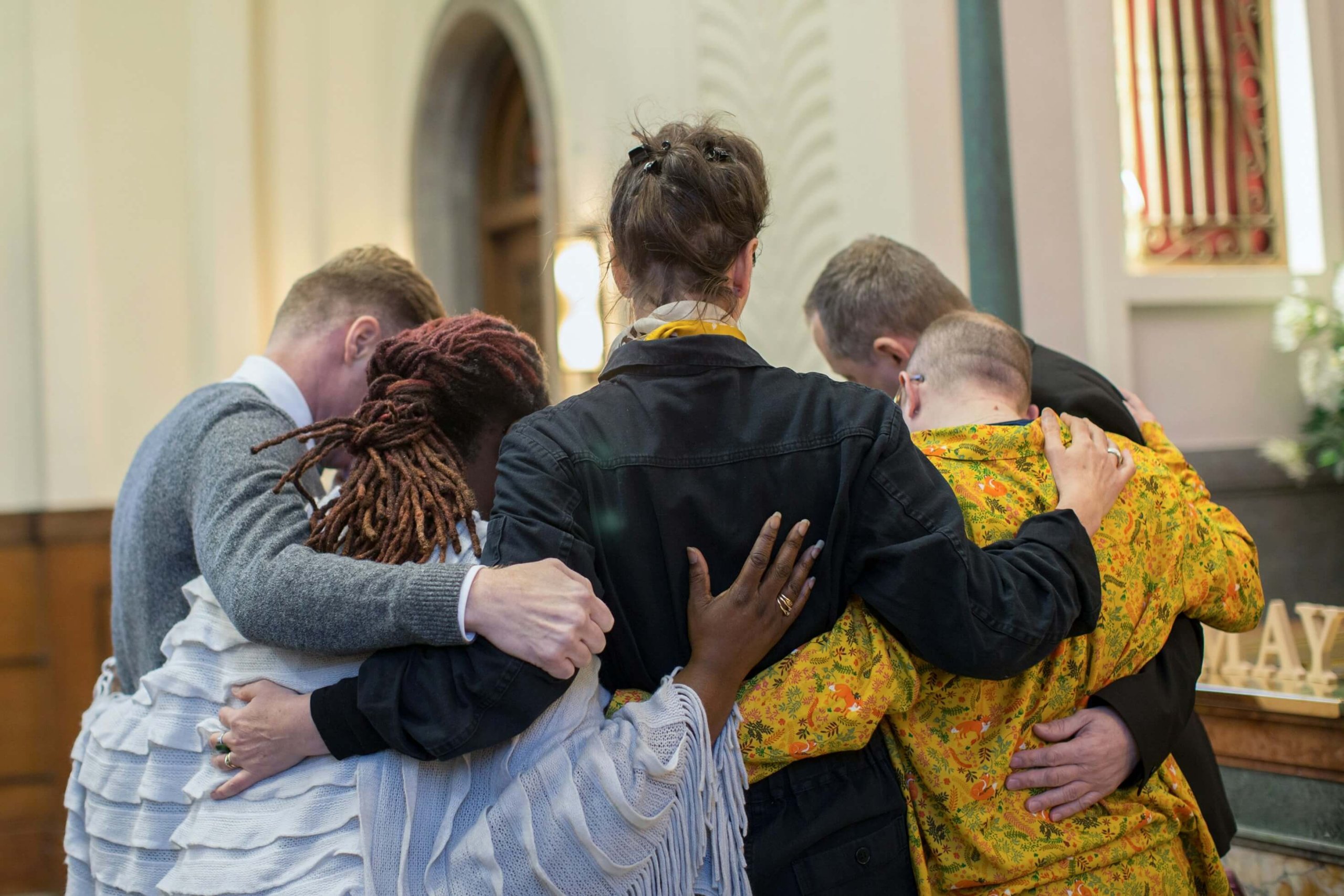A circle of individuals embracing in a church setting, representing the power of community support during loss and grief in Scotch Plains, NJ. What does grieving mean in practice? Finding safe spaces to process emotions with others who understand. Grief counseling NJ offers compassionate care for grieving symptoms in Branchburg, NJ and Scotch Plains.