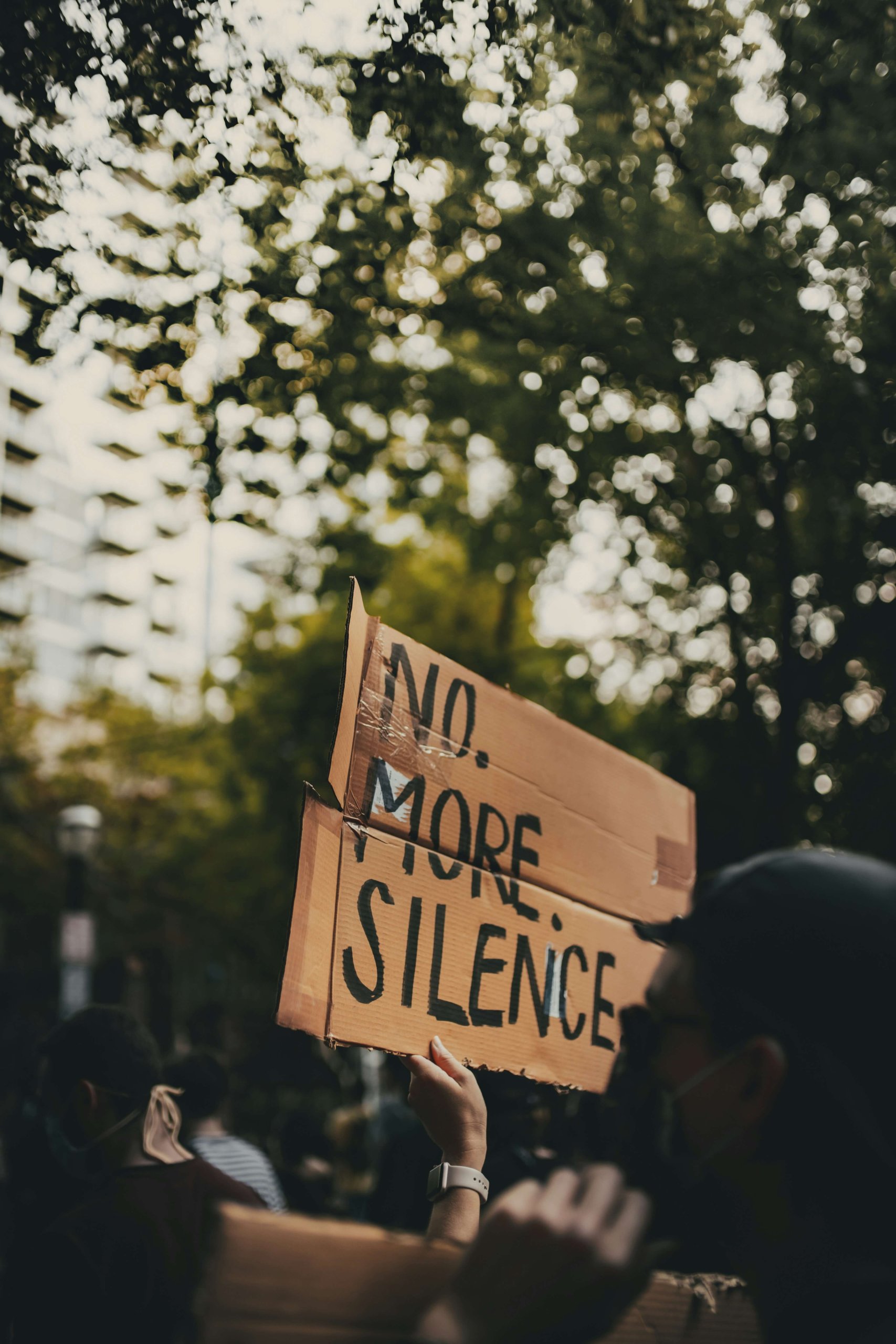 Protest sign reading "No More Silence" held outdoors, symbolizing collective grief and moral injury from current events in Branchburg. Serving Branchburg, Scotch Plains, and Somerville, Brave Minds provides grief counseling to help process distress from ongoing national issues and social media exposure.