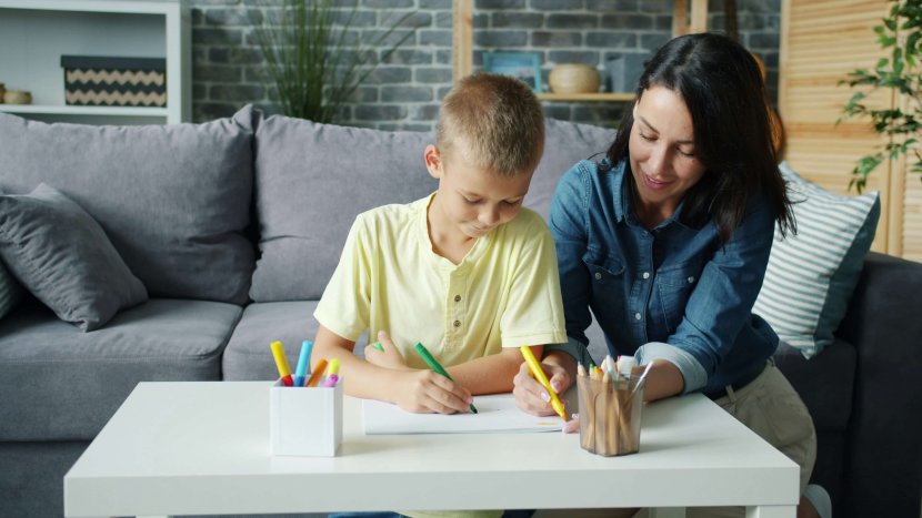 A smiling mother sits beside her son as he draws with colorful markers at a white table, capturing the essence of emotional wellness NJ in Somerville. Serving Somerville, Branchburg, and Scotch Plains — providing emotional regulation skills NJ families can use to nurture emotional growth NJ children deserve.