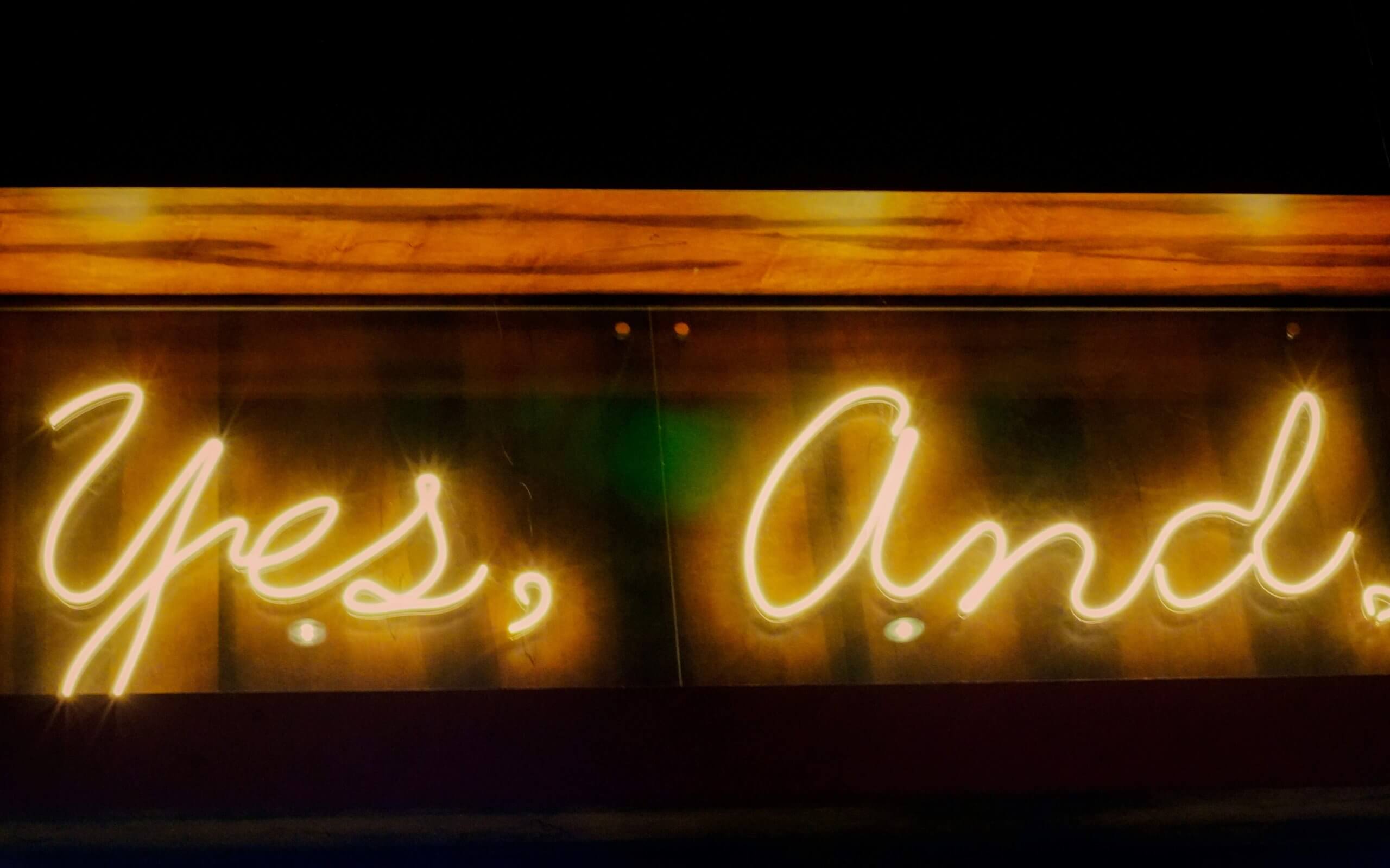 A neon "Yes, And" sign representing the improv-inspired validation technique used by our child therapist in Branchburg, NJ. Serving Scotch Plains and Branchburg families seeking parent coaching and emotional validation strategies. 